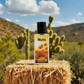 Blissful Floral Temptation perfume bottle on straw bale with desert cactus and blue sky background