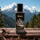 Blissful Millionaire perfume bottle on wooden surface with mountain and pine tree background