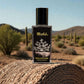 Blissful Millionaire perfume bottle on textured surface with desert landscape and cacti background
