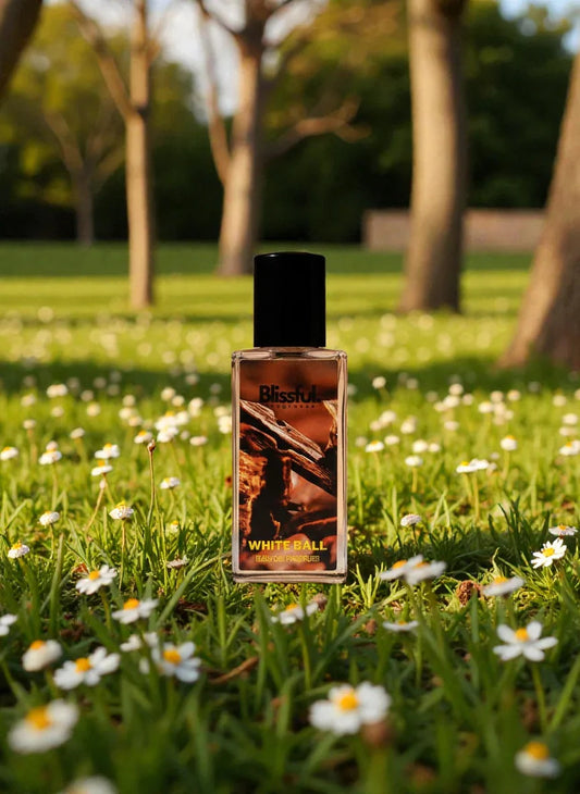 Blissful fragrance bottle labeled White Ball placed on grass with white daisies in a sunlit park
