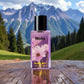 Blissful Blue Lady perfume bottle with pink flowers on wooden surface, mountainous background